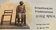 Auf dem Bild ist ein leerer Bronzestuhl und daneben die auf einem Stuhl sitzende Statue einer jungen Frau
