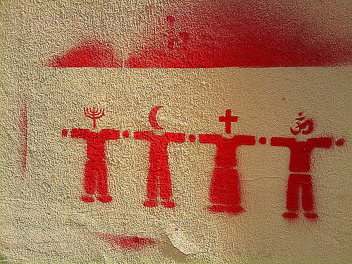 Streetart mit interreligiösen Symbolen, rotes Grafitti auf graubraunem Rauputz