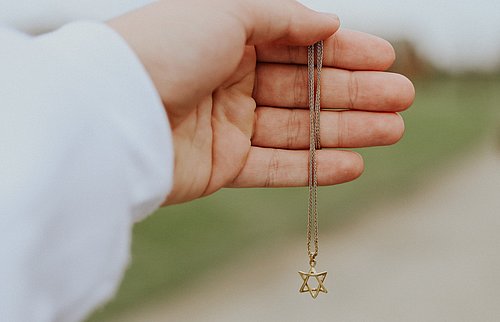 Eine Hand hält eine goldenen Kette mit einem Davidstern-Anhänger in die Kamera