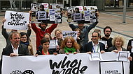 Auf dem Bild sind menschen zu sehen, die Schilder mit der Aufschrift "who made my clothes" hochhalten.