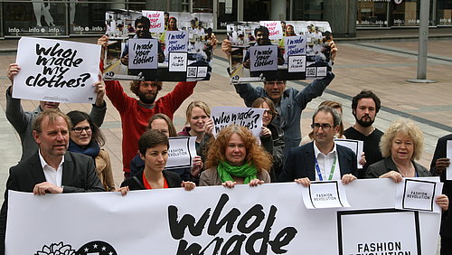 Auf dem Bild sind menschen zu sehen, die Schilder mit der Aufschrift "who made my clothes" hochhalten.