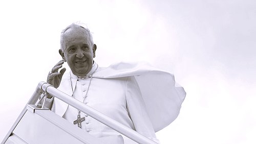 Das Bild zeigt Papst Franziskus 2015 bei einer seiner Reisen auf der Treppe eines Flugzeuges stehend und winkend