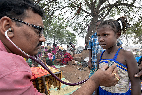 Auf dem Platz, auf dem ueblicherweise die Waste-Picker Berge von Plastikmuell sortieren, hat DBRC (Dalit Bahujan Resource Center) ein Health Camp fuer die Waste-Picker Familien eingerichtet. Der Arzt Dr. Boda Srinivas (37 Jahre) der "staatlichen Gesundheits und Familienfuersorge" hoert mit einem Stethoskop die Bronchien eines Maedchens ab.