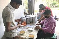 Das Bild zeigt Männer in Indien, die verzehrfertige Mahlzeiten zum Mitnehmen für Bedürftige verpacken.