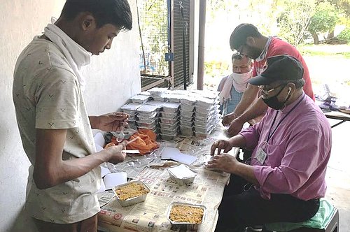 Das Bild zeigt Männer in Indien, die verzehrfertige Mahlzeiten zum Mitnehmen für Bedürftige verpacken.